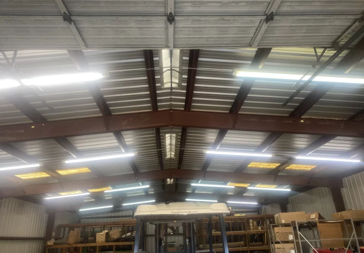 Interior of an industrial warehouse with high ceilings and multiple rows of fluorescent lights illuminating the space.