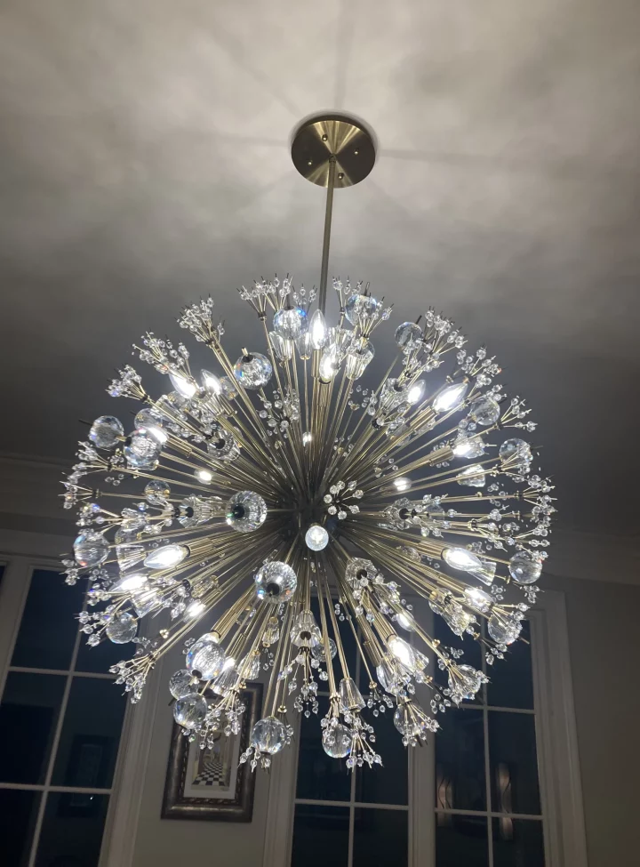 Luxurious chandelier with multiple crystal embellishments and radiant lights, hanging from the ceiling of a well-decorated room.
